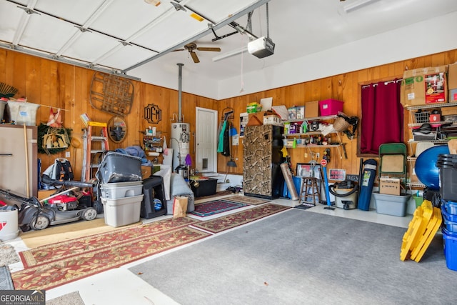 garage featuring a garage door opener, wooden walls, ceiling fan, and water heater