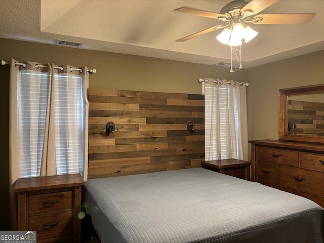 bedroom with a textured ceiling, ceiling fan, and wood walls