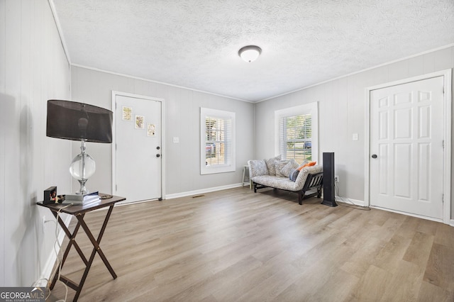 living area featuring crown molding, light hardwood / wood-style flooring, and a textured ceiling