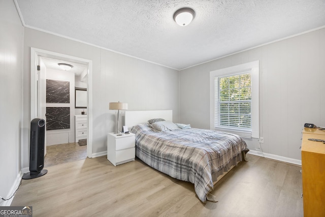 bedroom with crown molding, connected bathroom, light hardwood / wood-style floors, and a textured ceiling