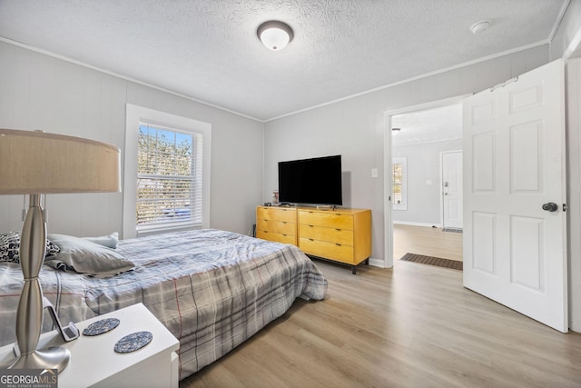 bedroom featuring ornamental molding, a textured ceiling, and light hardwood / wood-style floors