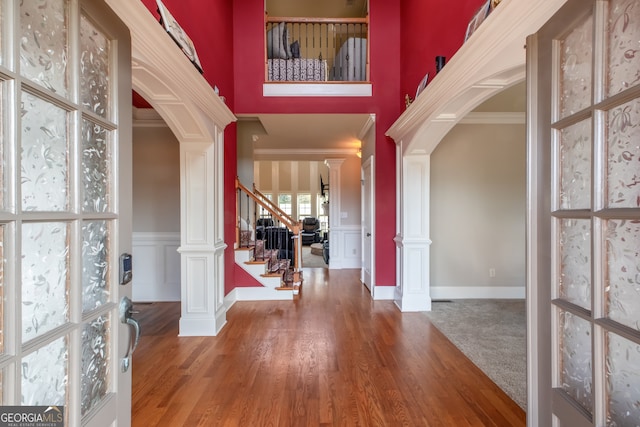 entryway with crown molding, a high ceiling, hardwood / wood-style floors, and ornate columns