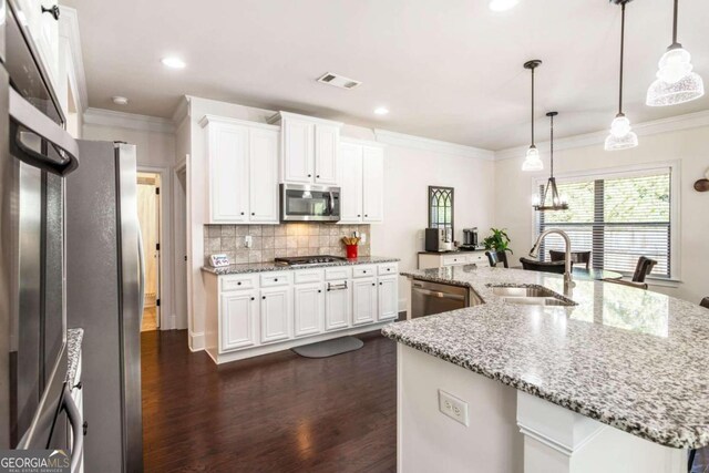 kitchen featuring appliances with stainless steel finishes, white cabinets, pendant lighting, a center island with sink, and sink