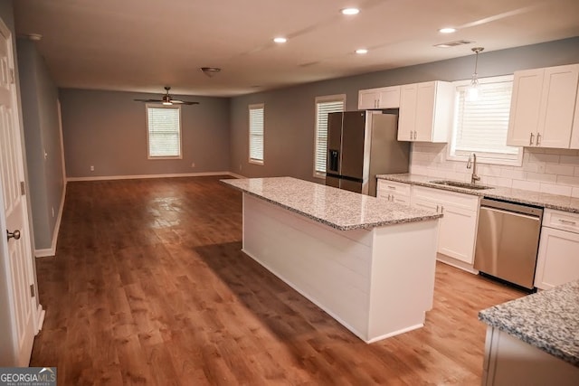 kitchen with appliances with stainless steel finishes, hanging light fixtures, white cabinetry, a center island, and sink