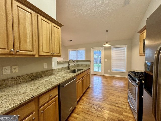 kitchen featuring light stone counters, lofted ceiling, sink, appliances with stainless steel finishes, and light wood-type flooring