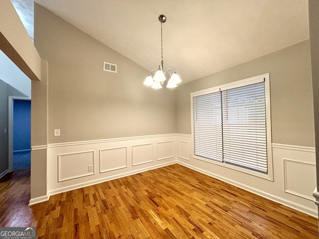 empty room featuring a chandelier, vaulted ceiling, and hardwood / wood-style flooring