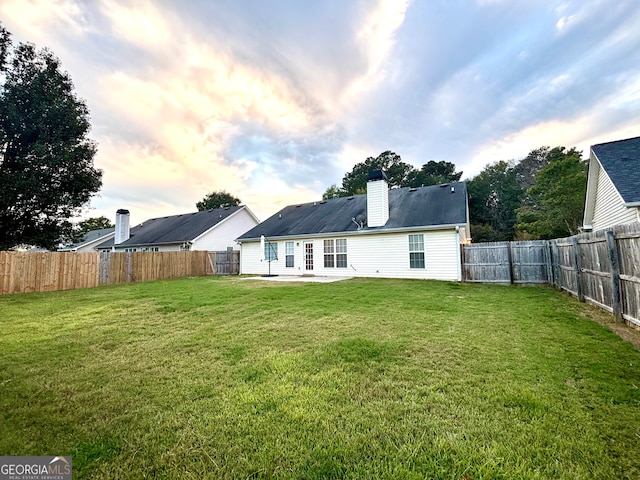 back house at dusk with a lawn and a patio area