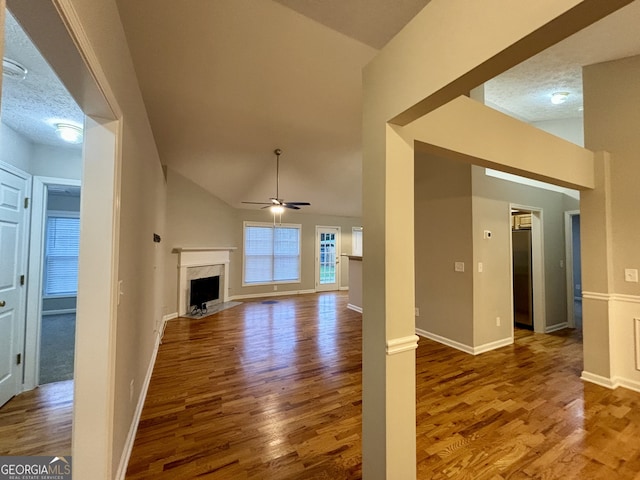 unfurnished living room featuring ceiling fan, lofted ceiling, a textured ceiling, hardwood / wood-style flooring, and a fireplace