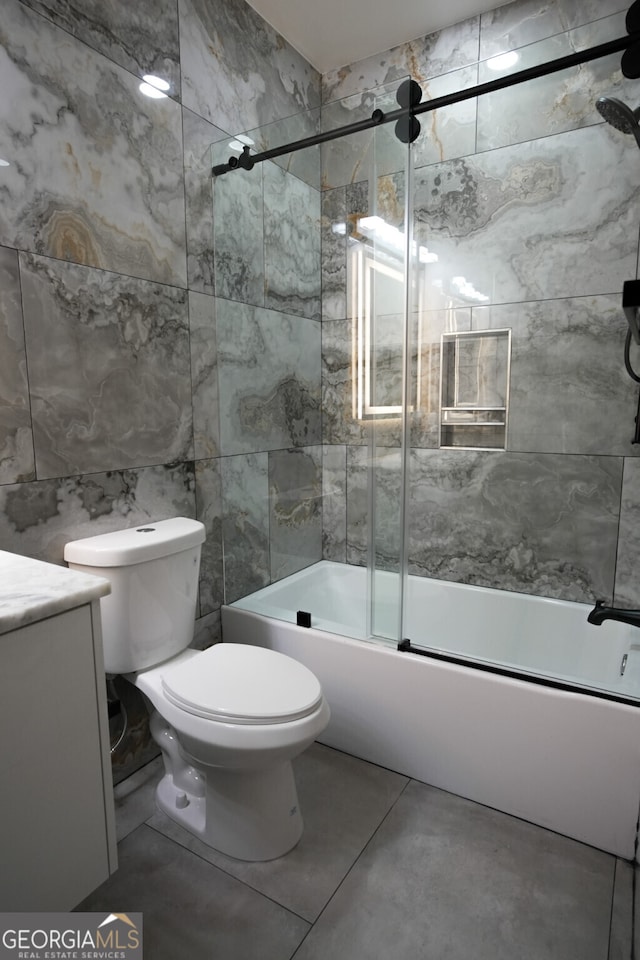 full bathroom featuring bath / shower combo with glass door, vanity, tile walls, and toilet