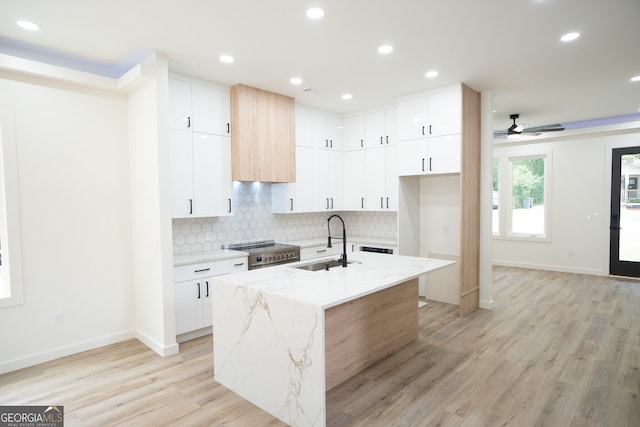 kitchen featuring light hardwood / wood-style floors, sink, white cabinetry, a center island with sink, and light stone countertops