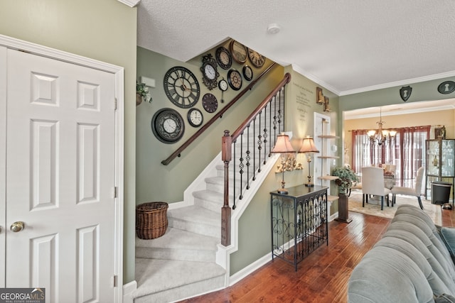 stairs featuring a notable chandelier, a textured ceiling, hardwood / wood-style flooring, and ornamental molding