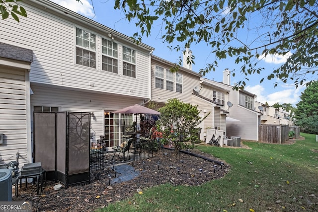 rear view of house featuring central AC unit and a lawn