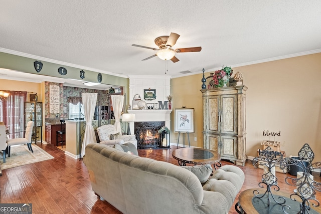 living room with a high end fireplace, a textured ceiling, hardwood / wood-style floors, crown molding, and ceiling fan