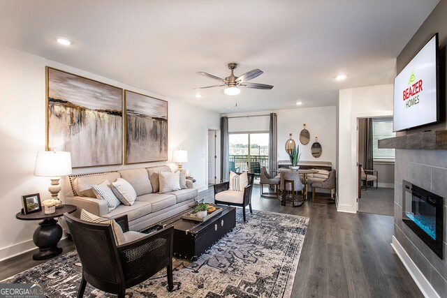 living room featuring a tiled fireplace, ceiling fan, and dark wood-type flooring