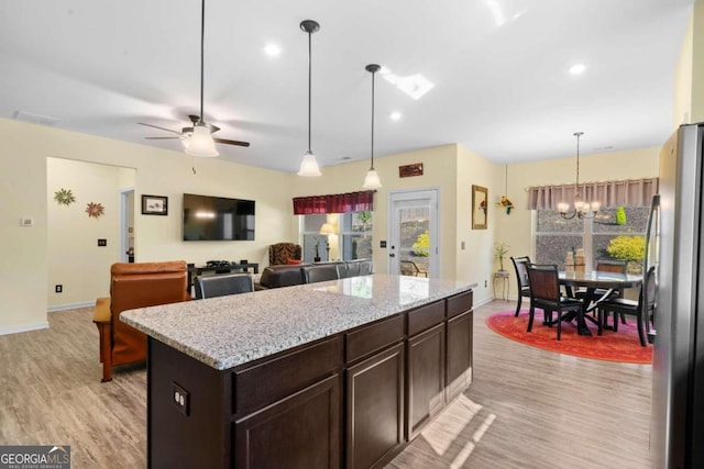 kitchen with a kitchen island, hanging light fixtures, stainless steel refrigerator, light hardwood / wood-style flooring, and dark brown cabinets