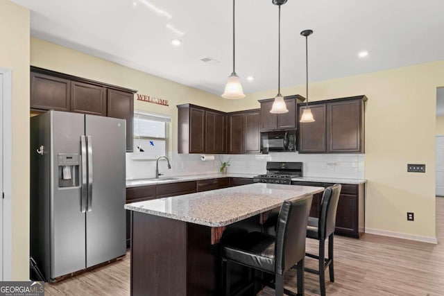 kitchen with hanging light fixtures, light hardwood / wood-style floors, light stone counters, a kitchen island, and black appliances