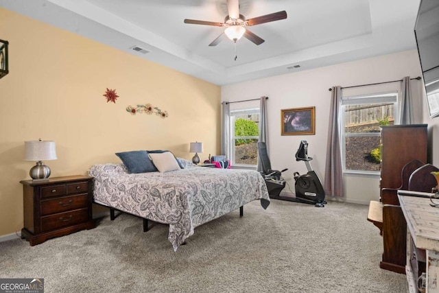 bedroom with ceiling fan, a raised ceiling, and light carpet