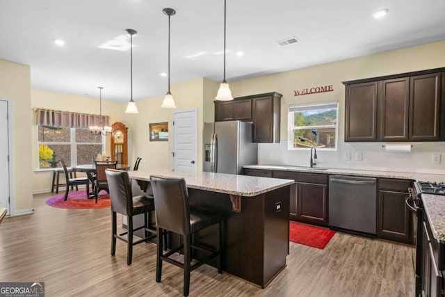 kitchen with pendant lighting, appliances with stainless steel finishes, a kitchen island, light hardwood / wood-style flooring, and a breakfast bar area