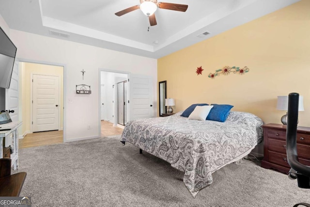 bedroom with ceiling fan, light colored carpet, and a tray ceiling