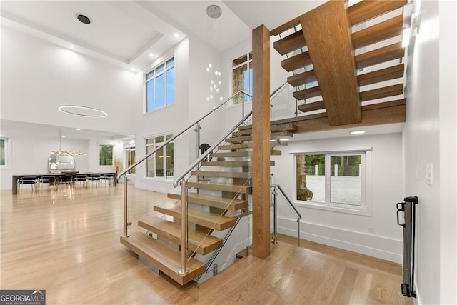 staircase featuring a notable chandelier, a towering ceiling, and hardwood / wood-style floors