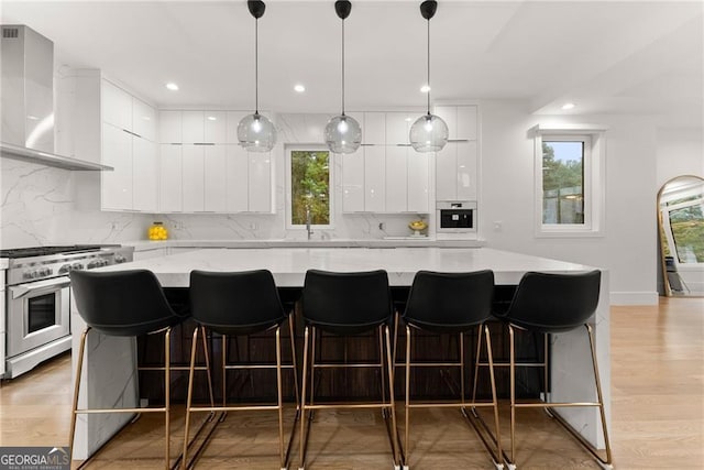 kitchen with light hardwood / wood-style floors, wall chimney exhaust hood, stainless steel appliances, light stone countertops, and a spacious island