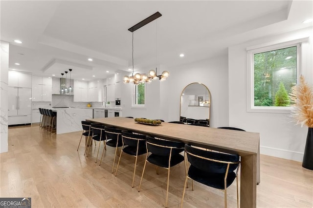 dining room with light wood-type flooring, a raised ceiling, and a chandelier