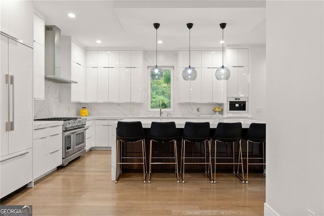 kitchen featuring light hardwood / wood-style flooring, white cabinets, wall chimney range hood, and high quality appliances