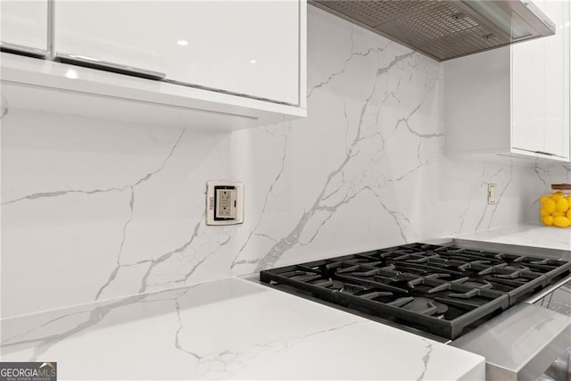 kitchen featuring range with gas cooktop, white cabinets, wall chimney range hood, backsplash, and light stone countertops