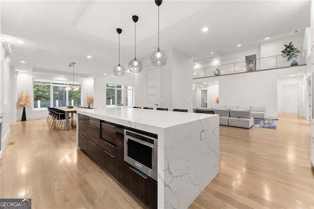 kitchen with hanging light fixtures, light hardwood / wood-style floors, light stone countertops, dark brown cabinetry, and a large island