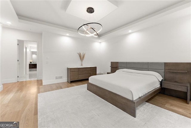 bedroom with light wood-type flooring, a raised ceiling, and an inviting chandelier