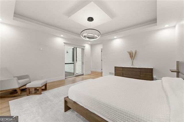 bedroom with an inviting chandelier, a raised ceiling, and hardwood / wood-style floors