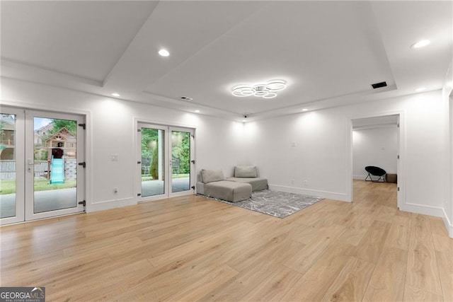 unfurnished room with light wood-type flooring, a raised ceiling, and french doors