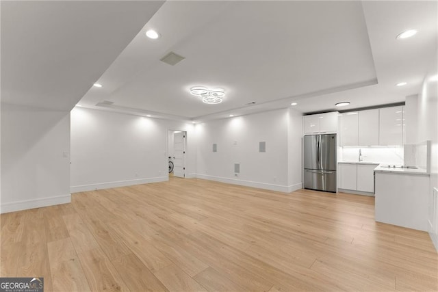 unfurnished living room with light hardwood / wood-style floors, a tray ceiling, and sink