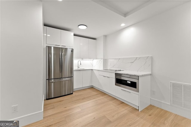 kitchen with backsplash, light hardwood / wood-style flooring, stainless steel appliances, and white cabinets