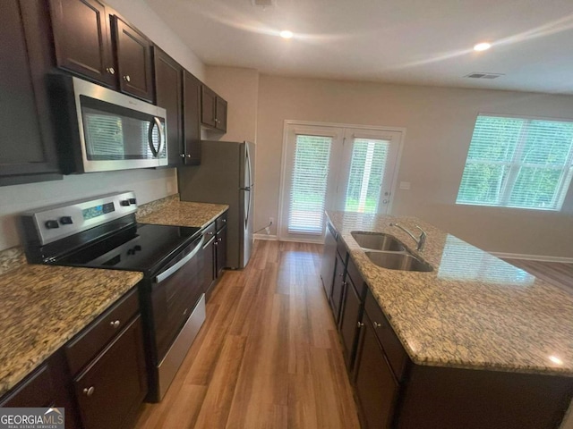 kitchen featuring light stone counters, sink, a center island with sink, light hardwood / wood-style flooring, and appliances with stainless steel finishes