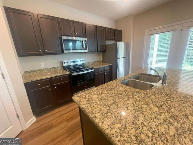 kitchen with appliances with stainless steel finishes, light stone countertops, light wood-type flooring, dark brown cabinets, and sink