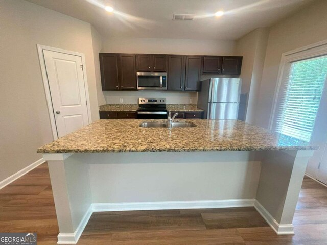 kitchen with appliances with stainless steel finishes, a kitchen island with sink, sink, and dark hardwood / wood-style floors