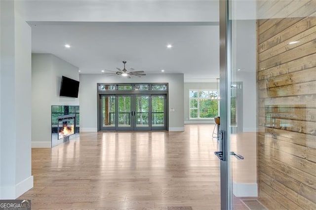 unfurnished living room featuring light hardwood / wood-style flooring, ceiling fan, and wooden walls