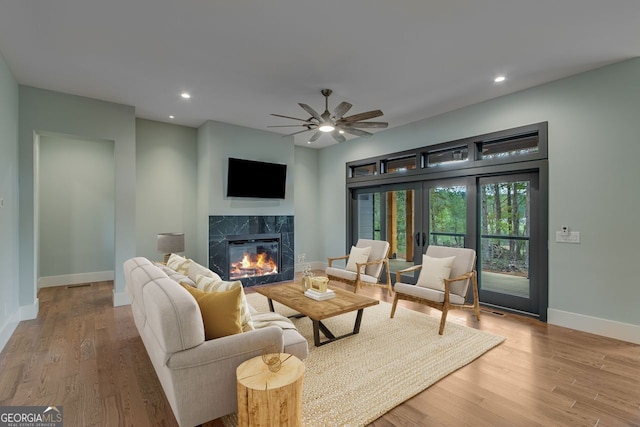 living room featuring ceiling fan, a high end fireplace, and light hardwood / wood-style floors