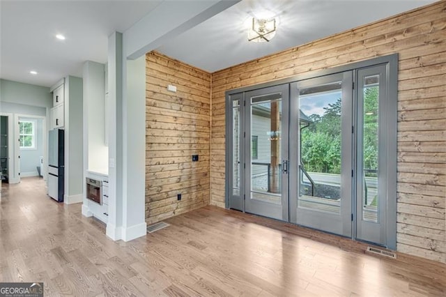 doorway featuring wood walls, light wood-type flooring, and french doors