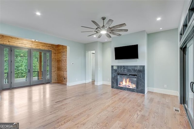 unfurnished living room featuring ceiling fan, french doors, a high end fireplace, and light hardwood / wood-style floors