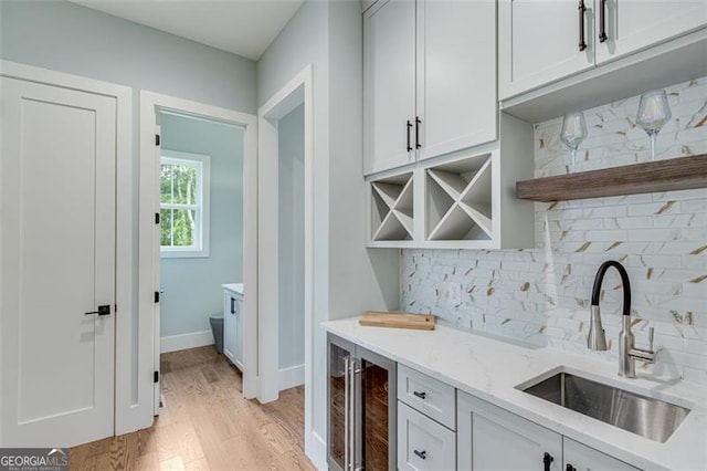 bar featuring light stone counters, white cabinets, decorative backsplash, beverage cooler, and sink