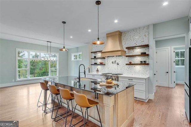 kitchen with white cabinetry, decorative light fixtures, premium range hood, backsplash, and a breakfast bar area