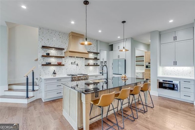 kitchen featuring a center island with sink, stove, premium range hood, white cabinetry, and a kitchen bar