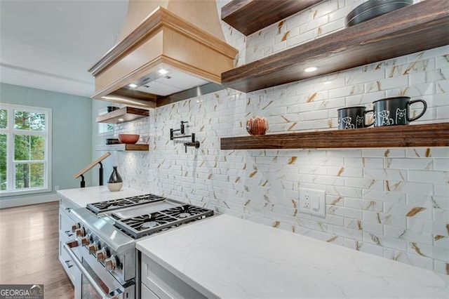 kitchen featuring light wood-type flooring, light stone counters, high end stainless steel range oven, and backsplash