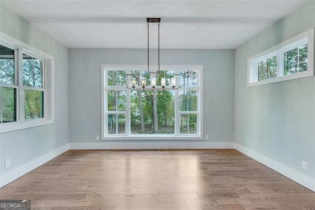 unfurnished dining area with light hardwood / wood-style flooring, a chandelier, and a healthy amount of sunlight