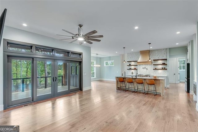 kitchen featuring light hardwood / wood-style flooring, hanging light fixtures, premium range hood, an island with sink, and a kitchen bar