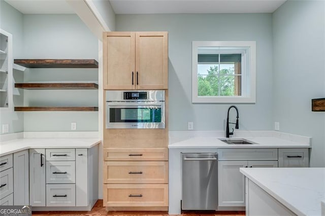 kitchen with sink, stainless steel oven, light stone countertops, and light brown cabinetry