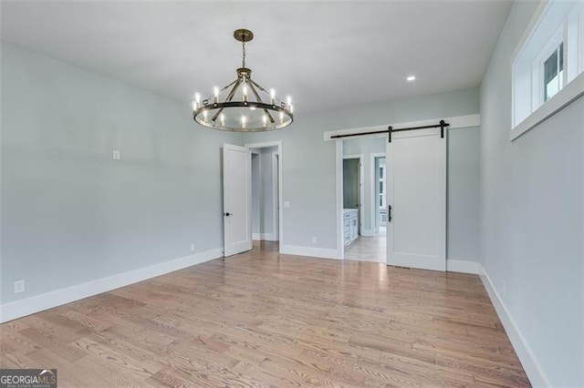 empty room with light wood-type flooring, a chandelier, and a barn door