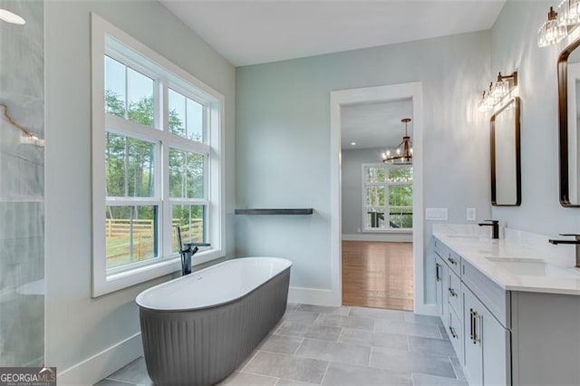 bathroom featuring a bathing tub, vanity, an inviting chandelier, and a healthy amount of sunlight